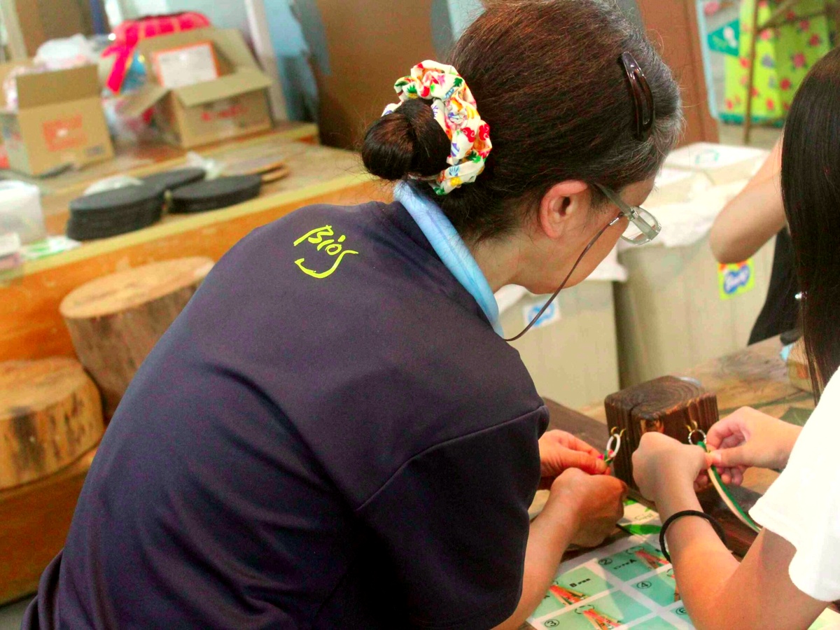 ビオスの丘のかんたん革細工体験で、専門講師のレクチャーを受けながら本革を編み込む参加者の様子。